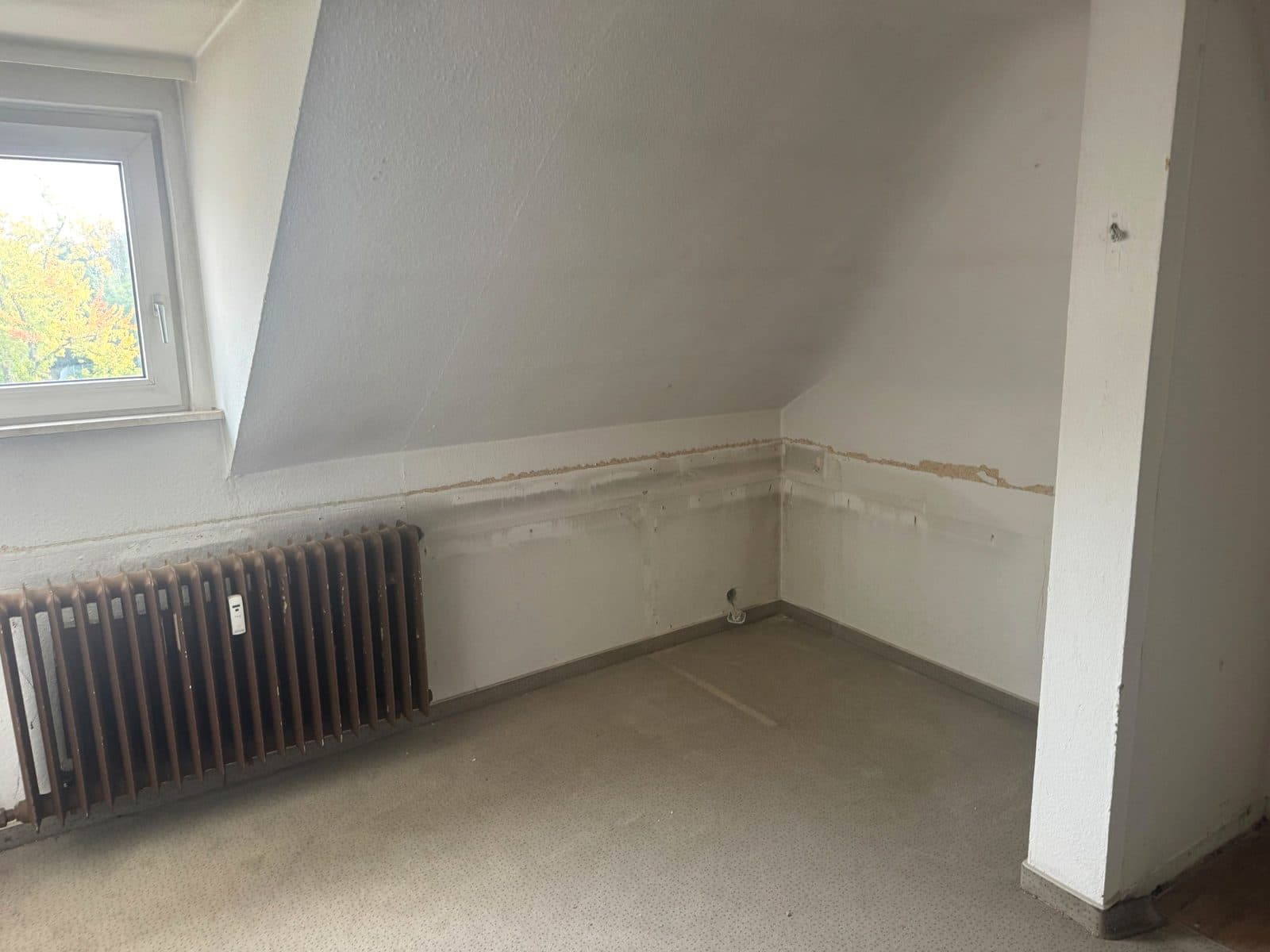 Geräumtes Dachgeschosszimmer mit Heizkörper nach der Entrümpelung