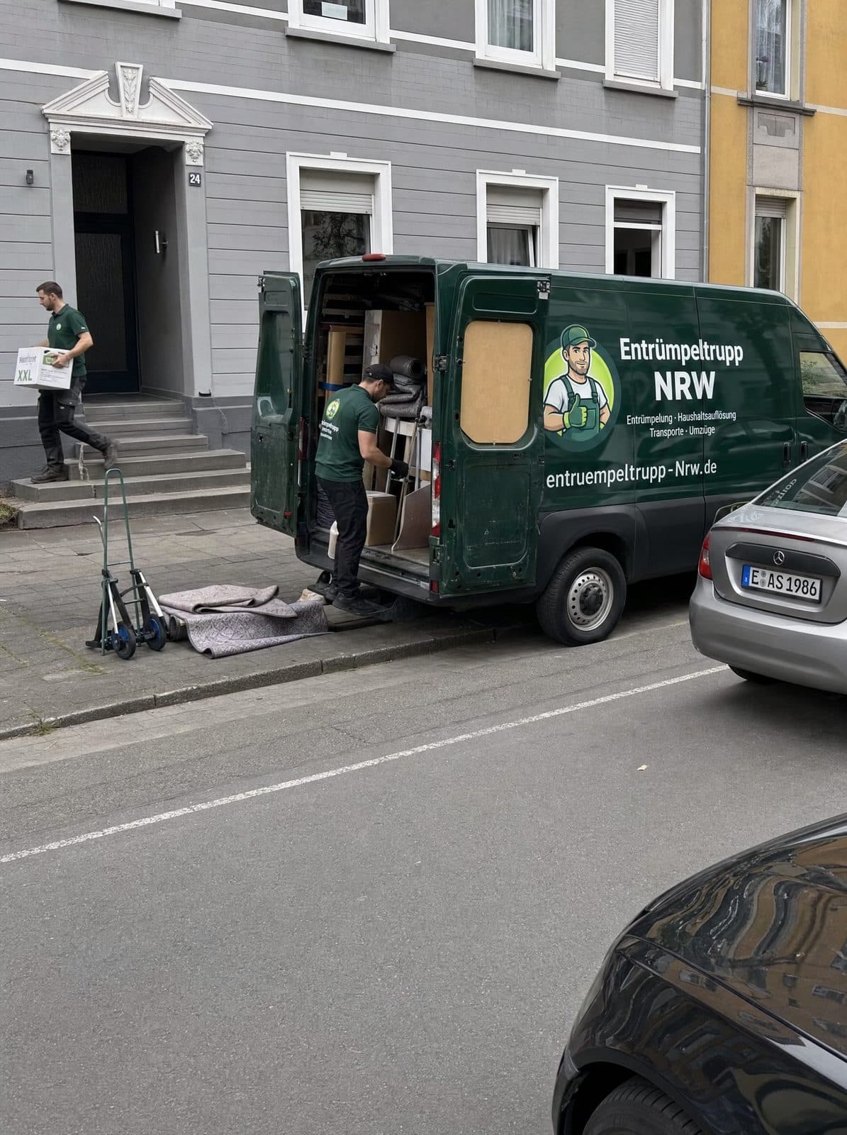 Team von Entrümpeltrupp NRW trägt Möbel und Kartons aus einem Altbau in Essen zum Transporter