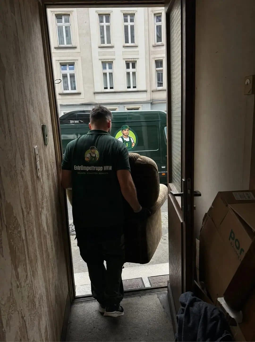 Mitarbeiter von Entrümpeltrupp NRW trägt einen Sessel aus einem Altbau in Essen zum Firmentransporter